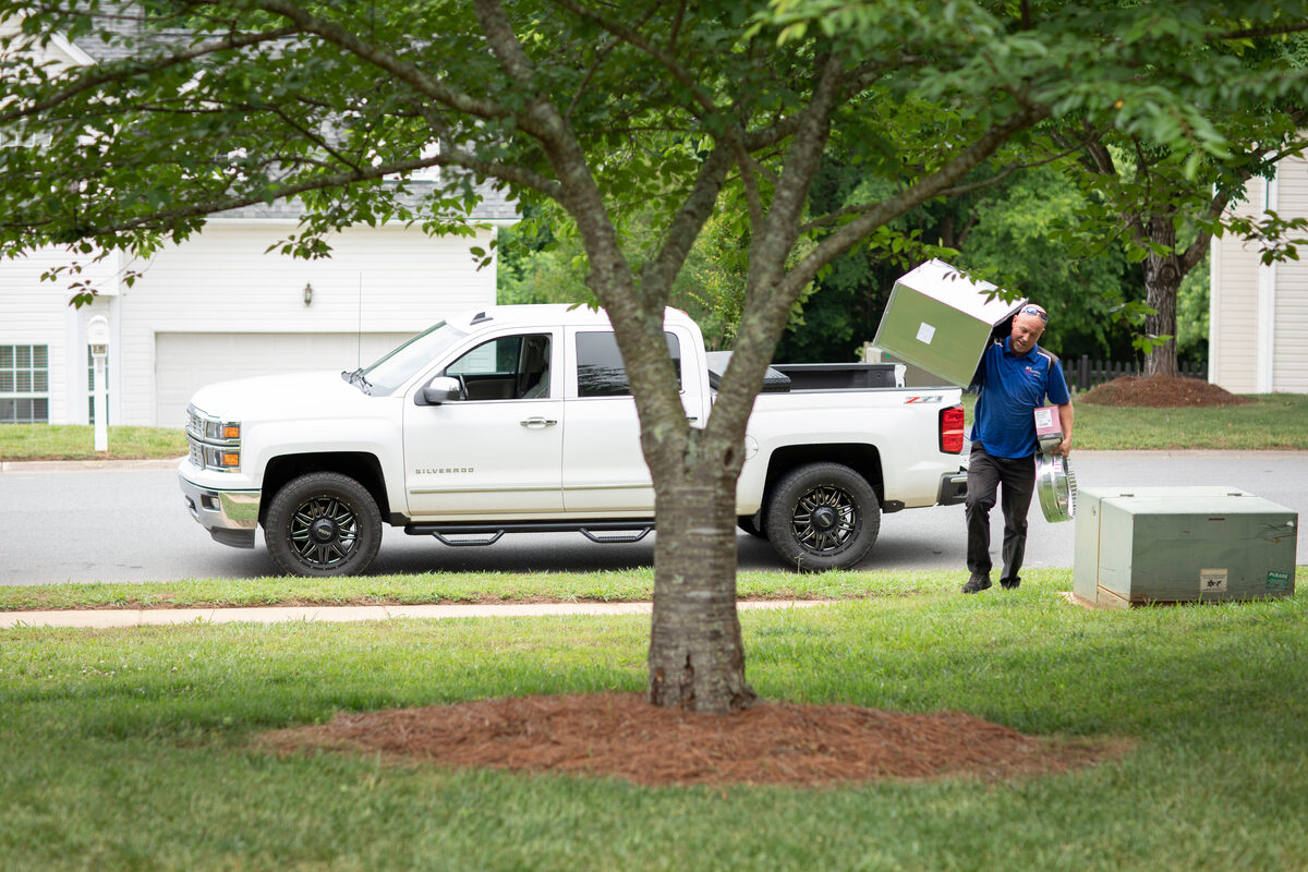 HVAC technician carrying equipment outside a home